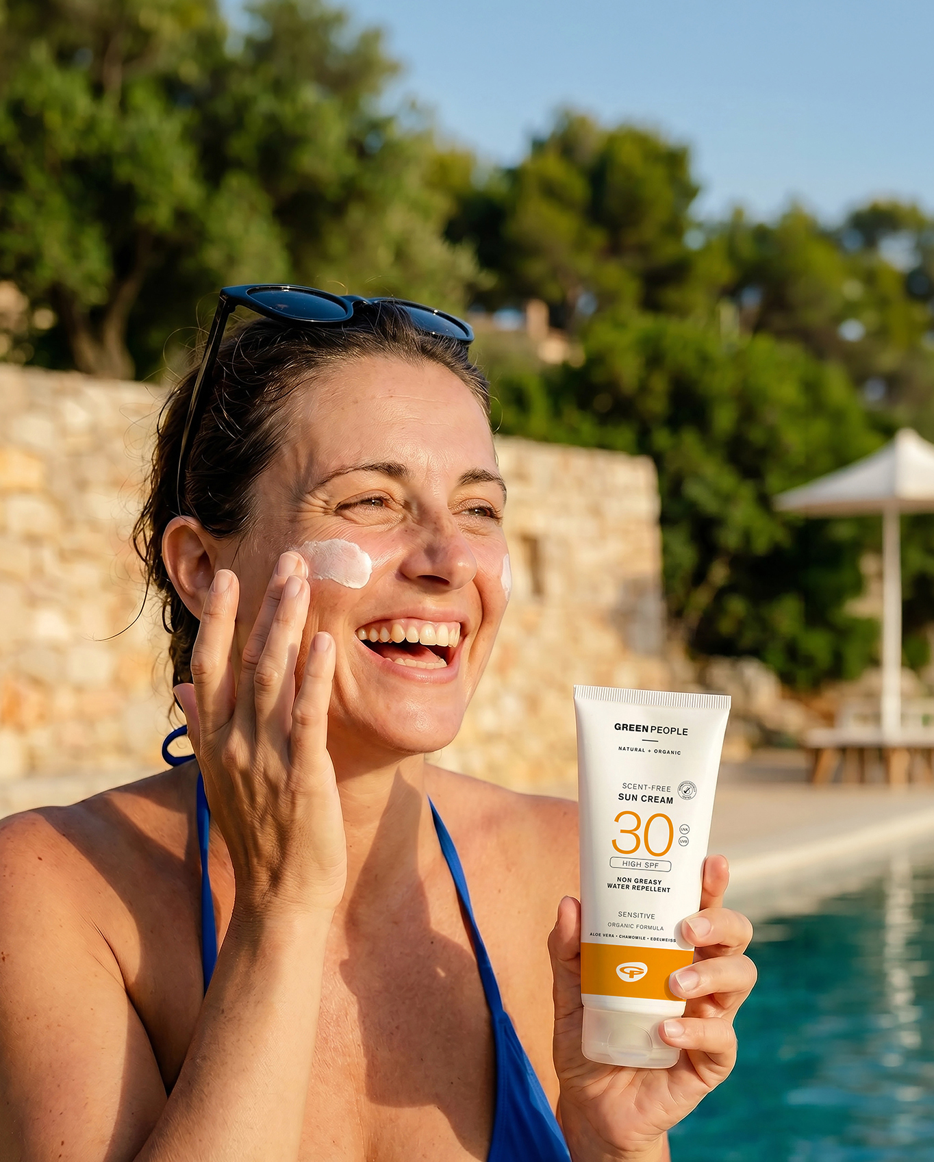 Woman applying Green People Scent Free Sun Cream SPF30 by a pool
